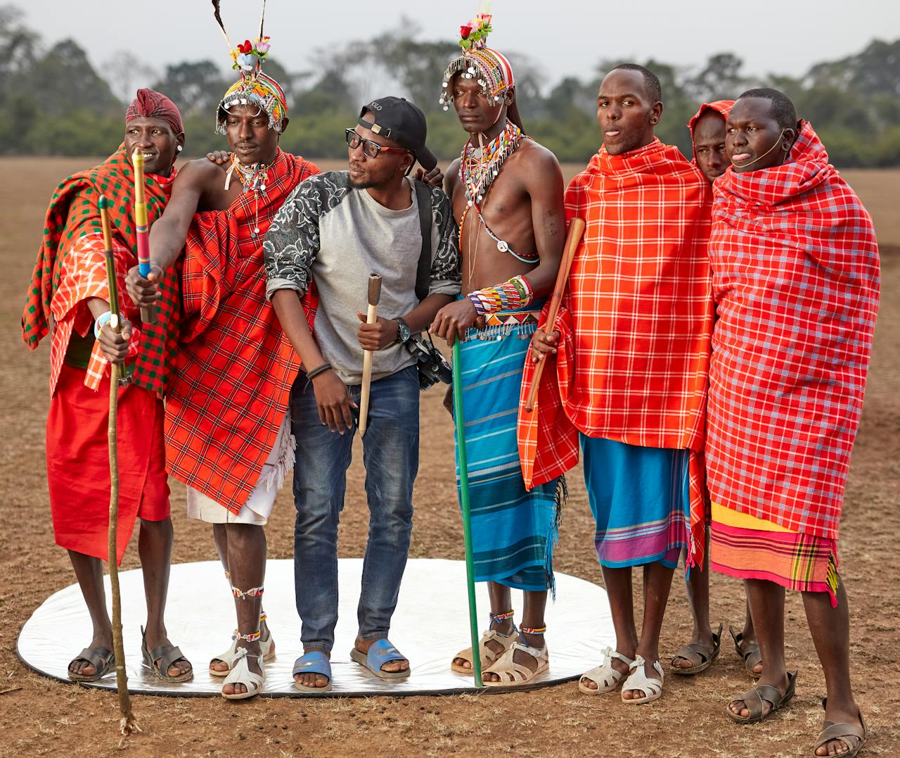 A group of Maasai men in traditional attire alongside a photographer outdoors.