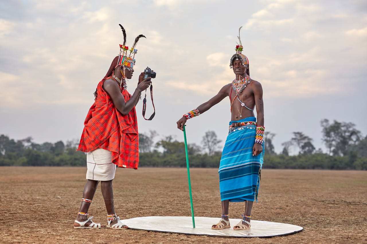 hero-img-01 Two Maasai men in traditional attire with a camera in a natural setting.