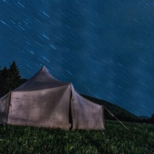 A serene night camping scene with a tent under star trails in the mountains.
