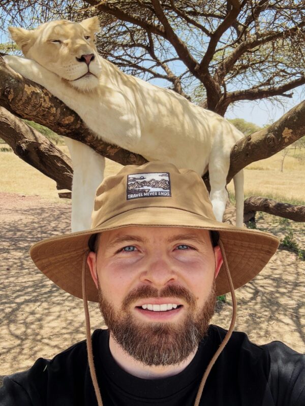 A man with a hat takes a selfie under a white lion resting on a tree in Kilimanjaro, Tanzania.