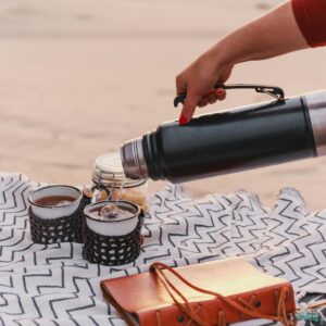 A peaceful outdoor setting with a thermos pouring tea into mugs on a blanket in the Namibian desert.